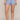 A model wearing light blue pajama shorts with a small dark blue floral print, shown from the waist down against a solid beige studio background.