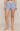 A model wearing light blue pajama shorts with a small dark blue floral print, shown from the waist down against a solid beige studio background.