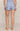 Rear view of a model wearing light blue high-waisted shorts with a dark blue floral pattern, paired with a matching top, against a solid beige studio background.