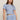 A woman modeling a light blue short-sleeve crop top and matching drawstring pants set with a small dark floral print, against a plain beige studio background.