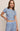 A woman modeling a light blue short-sleeve crop top and matching drawstring pants set with a small dark floral print, against a plain beige studio background.