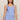 A woman modeling a light blue ribbed knit sleeveless top and matching pants against a plain beige studio background.