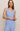 A woman modeling a light blue ribbed knit two-piece set consisting of a sleeveless tank top and matching pants, photographed against a plain beige studio background.