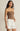 Woman wearing a strapless brown top and white shorts on a beige background