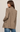 A woman shown from the back wearing an oversized brown and beige houndstooth blazer with blue jeans, photographed against a plain light beige studio background.
