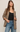 A woman modeling a brown and beige houndstooth blazer over a black tank top and blue jeans, standing against a plain light beige studio background.