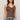 Woman wearing a brown tank top with lace details and blue jeans on a beige background