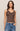 Woman wearing a brown tank top with lace details and blue jeans on a beige background