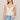 Woman wearing a white lace tank top and blue jeans against a plain background