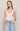 Woman wearing a white lace tank top and blue jeans against a plain background