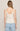A woman viewed from the back wearing a light cream camisole tank top with lace trim and light blue jeans, set against a plain light beige studio background.