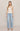 A woman modeling a light beige lace-trimmed camisole top and light-wash wide-leg jeans against a plain beige studio background.
