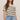 Woman wearing a beige sweater with black stripes and blue jeans on a plain background