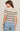 Woman wearing a beige sweater with black stripes and blue jeans on a plain background