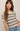 Woman wearing a beige and black striped sweater with blue jeans against a plain background