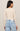 A woman shown from the back wearing a fitted long-sleeve cream top and light blue jeans against a plain light beige studio background.