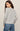 A woman shown from the back wearing a light gray long-sleeve top and blue jeans against a plain beige studio background.
