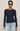 A woman modeling a navy blue long-sleeve knit top with a boat neckline, paired with light blue jeans, against a solid light gray background.