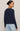 A woman shown from the back wearing a dark navy blue long-sleeve knit sweater and light wash blue jeans, set against a plain light beige studio background.