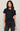 Woman wearing a black t-shirt and dark jeans against a plain background