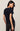 Woman wearing a black t-shirt and dark jeans against a plain background