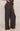 A person wearing dark brown wide-leg pleated pants, shown from the waist down against a plain light beige studio background.
