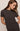 A woman wearing a dark brown ribbed short-sleeve crewneck top, shown from the waist up against a plain light beige background.