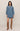 A model wearing a medium wash blue denim shirt dress with brown suede knee-high boots, standing against a solid beige studio background.