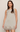 A woman modeling a sleeveless, light beige mini dress with a scalloped lace hem against a plain, light beige studio background.