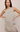 A woman modeling a sleeveless taupe-gray dress with a lace hem, posed against a neutral beige background.
