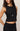 Woman wearing a black sleeveless top and skirt with a necklace on a plain background