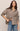 Woman wearing a brown checkered shirt and blue jeans on a beige background