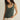 Woman wearing a green tank top and white pants against a beige background