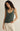 Woman wearing a green tank top and white pants against a beige background