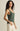 Woman wearing a green tank top and white pants against a beige background