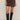 Person wearing a brown suede skirt and black knee-high boots on a beige background