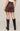 Person wearing a brown suede skirt and black knee-high boots on a beige background