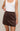 Person wearing a white tank top and brown skirt on a plain background