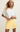Woman wearing a white top and yellow pleated skirt on a beige background