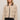 Woman wearing a beige jacket with dark collar and buttons on a plain background