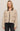 Woman wearing a beige jacket with dark collar and buttons on a plain background