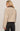 Woman wearing a beige jacket and black jeans against a plain background
