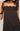 A close-up of a woman wearing a dark brown camisole top with black lace trim at the neckline and hem, against a light gray background.
