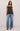 A woman modeling a dark brown camisole top with ruffle trim and wide-leg blue jeans against a plain light gray studio background.