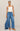 Woman wearing a white tank top and blue wide-leg jeans on a beige background