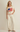 Woman wearing a cream-colored top with an American flag design and white pants on a beige background