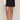A dark wash denim mini skirt with gold-tone hardware and contrast stitching, worn by a model in a cream knit sweater against a light gray studio background.
