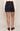 A person shown from the back wearing a dark blue denim mini skirt, a cream knit sweater, and dark brown loafers, against a plain light gray studio background.
