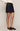 A model wearing a dark wash denim mini skirt with rolled hems, styled with a cream knit sweater and dark brown leather loafers against a plain beige studio background.