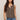 Woman wearing a brown sleeveless button-up shirt and blue jeans against a beige background